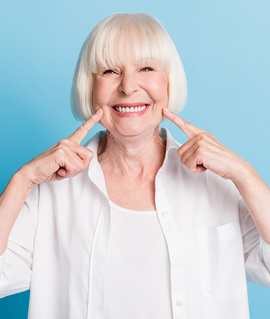 A smiling older woman with white hair, making a playful face with her fingers.