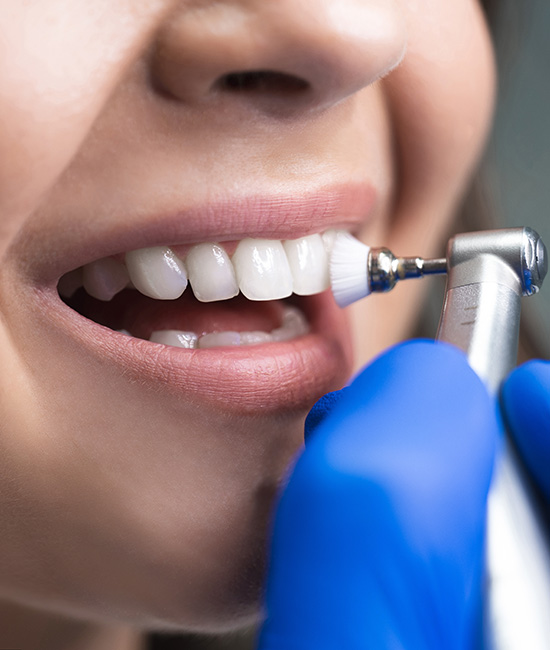 The image shows a person with their mouth open, engaging in the process of teeth cleaning or dental care, with an electric toothbrush being used, and they are smiling while wearing blue gloves.