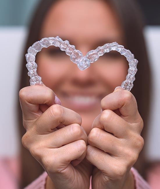 The image features a person holding up a pair of transparent braces, with their hands forming the shape of a heart.